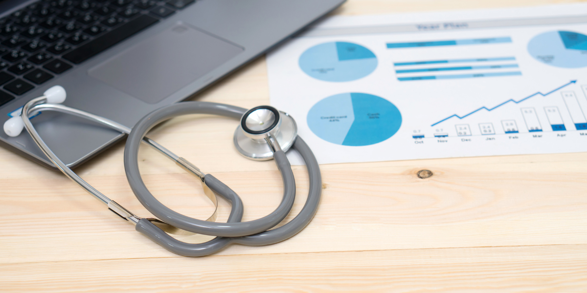 A stethoscope and laptop placed on a wooden table, symbolizing the intersection of healthcare and technology.