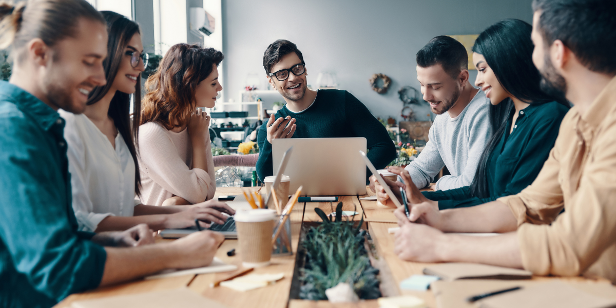 A diverse group of individuals collaborating at a table, each using laptops, in a professional setting.