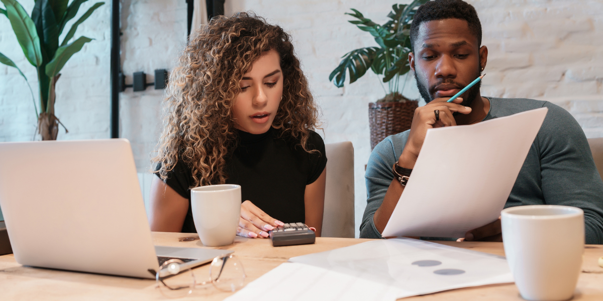 A man and woman collaborate at a table, reviewing a laptop and papers, discussing digital marketing budget strategies.