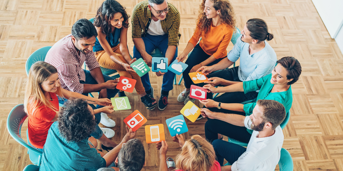 A diverse group of individuals engaged in discussion around a table adorned with vibrant social media icons.