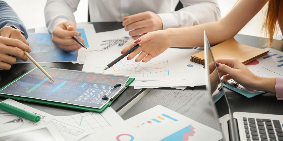 Business professionals collaborating on a laptop, surrounded by papers, illustrating teamwork and productivity in a corporate setting.